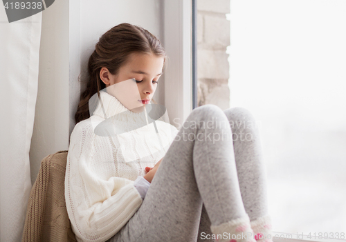 Image of sad girl sitting on sill at home window in winter
