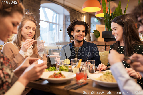 Image of friends with smartphones eating at restaurant