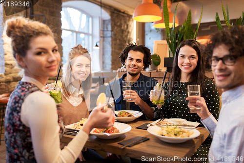 Image of happy friends eating and drinking at restaurant