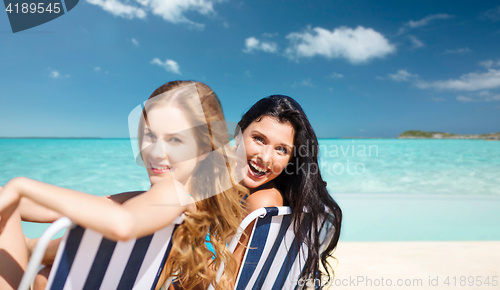 Image of happy women sunbathing in chairs on summer beach