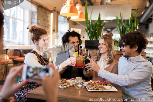 Image of happy friends clinking drinks at bar or cafe