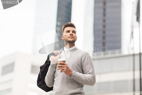 Image of young man with bag drinking coffee in city