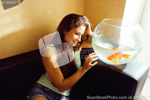 Image of pretty woman playing with goldfish at home, sunlight morning