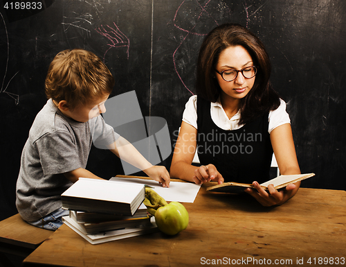 Image of little cute boy with young teacher in classroom studying at blac