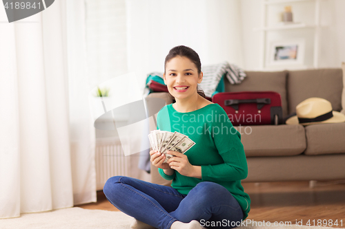 Image of happy woman with money and travel bag at home