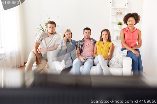 Image of sad friends watching tv at home