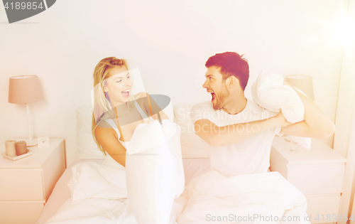 Image of happy couple having pillow fight in bed at home