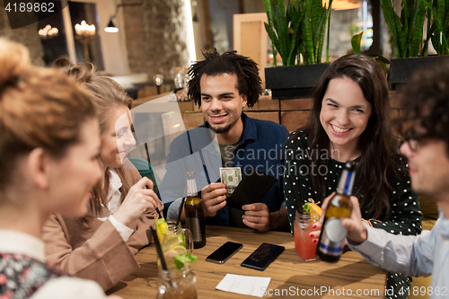 Image of friends with drinks, money and bill at bar