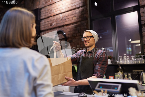 Image of woman taking paper bag from seller at cafe