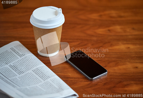 Image of coffee cup, smartphone and newspaper on table