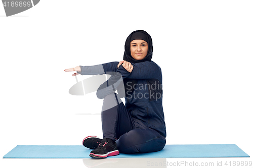 Image of muslim woman doing sportand stretching on mat