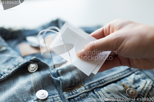 Image of close up of hand holding price tag of denim jacket