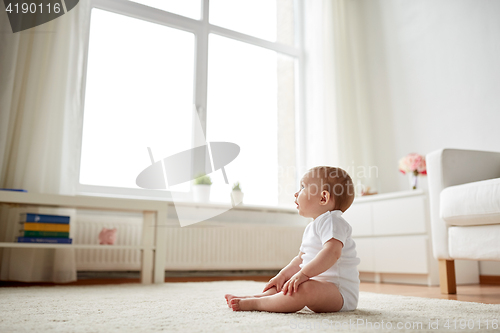 Image of happy baby boy or girl sitting on floor at home