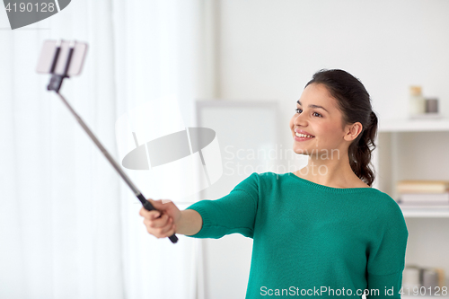 Image of woman taking selfie by smartphone monopod at home