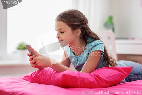 Image of smiling girl texting on smartphone at home