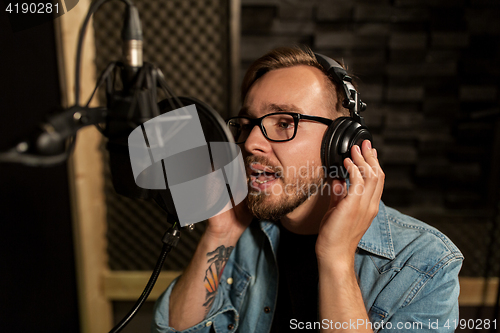 Image of man with headphones singing at recording studio