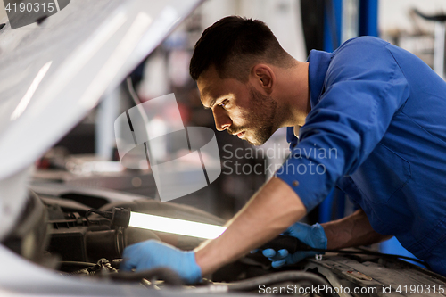 Image of mechanic man with lamp repairing car at workshop