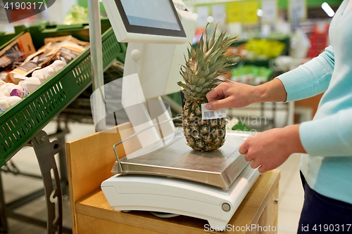 Image of woman weighing pineapple on scale at grocery store