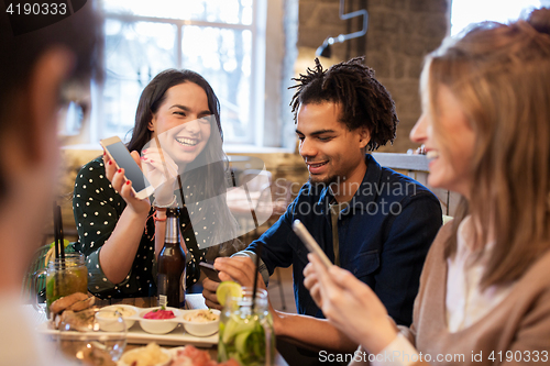 Image of friends with smartphones and food at bar or cafe