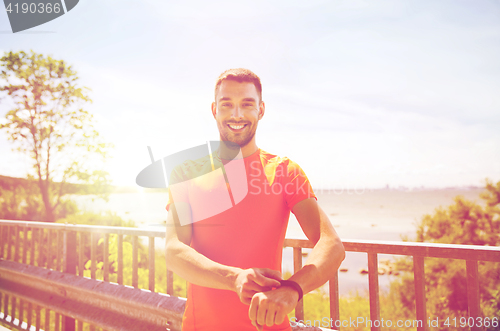 Image of smiling young man with smart wristwatch at seaside