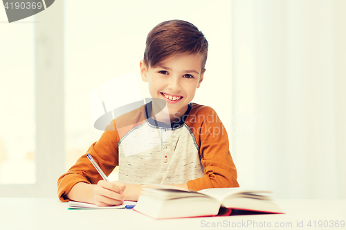 Image of smiling student boy writing to notebook at home
