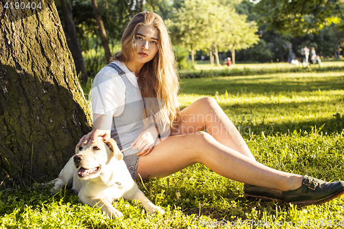 Image of young attractive blond woman playing with her dog in green park at summer, lifestyle people concept