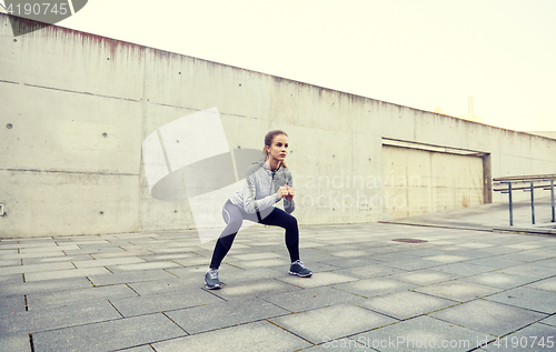 Image of happy woman doing squats and exercising outdoors