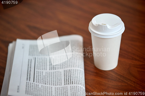 Image of coffee drink in paper cup and newspaper on table