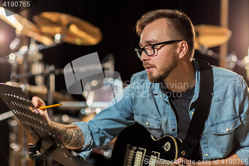 Image of man with guitar writing to music book at studio