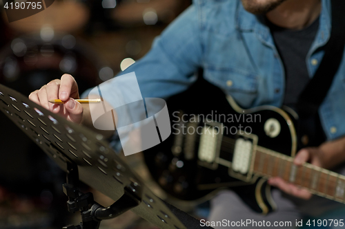 Image of man with guitar writing to music book at studio