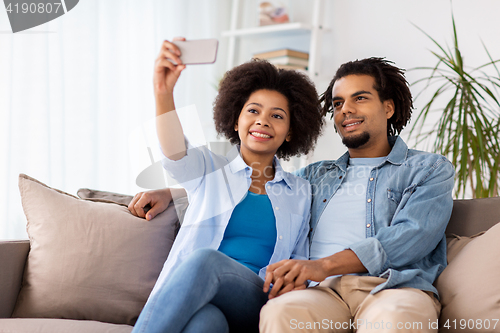 Image of happy couple with smartphone taking selfie at home