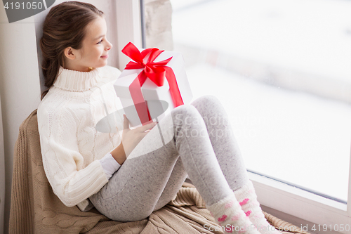 Image of girl with gift sitting on sill at home window