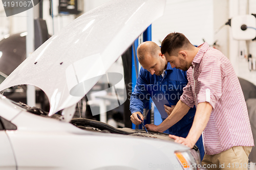 Image of auto mechanic with clipboard and man at car shop