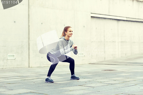 Image of happy woman doing squats and exercising outdoors