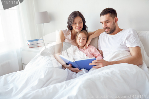 Image of happy family reading book in bed at home