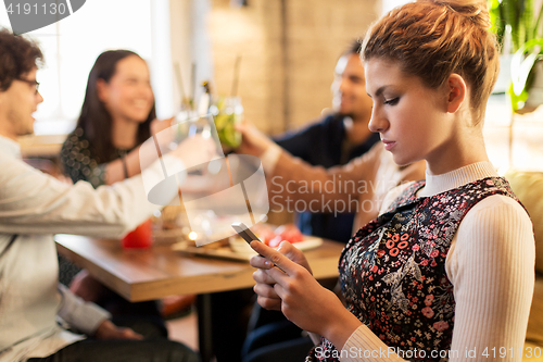 Image of woman with smartphone and friends at restaurant