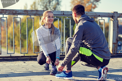 Image of smiling couple tying shoelaces outdoors