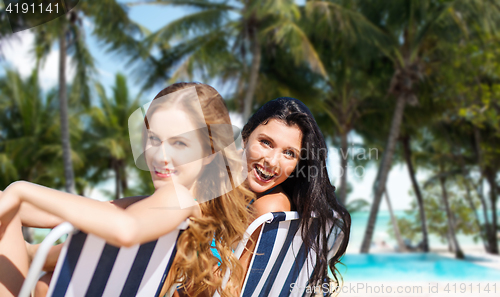 Image of happy women sunbathing in chairs on summer beach