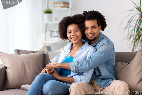 Image of happy couple sitting on sofa and hugging at home