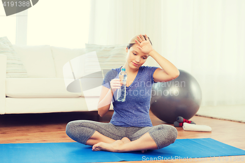 Image of tired woman drinking water after workout at home