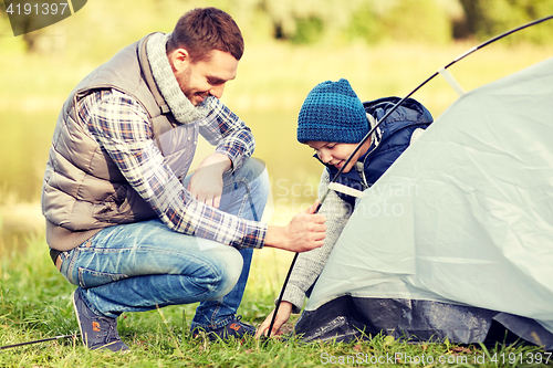 Image of happy father and son setting up tent outdoors