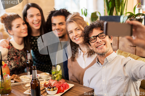 Image of friends taking selfie by smartphone at bar or cafe