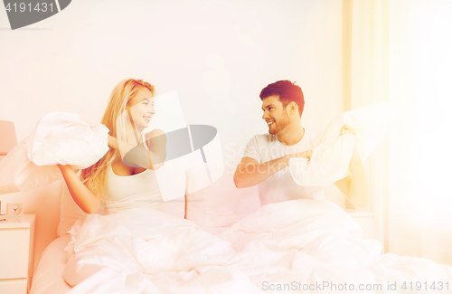 Image of happy couple having pillow fight in bed at home