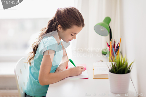 Image of happy girl with book writing to notebook at home