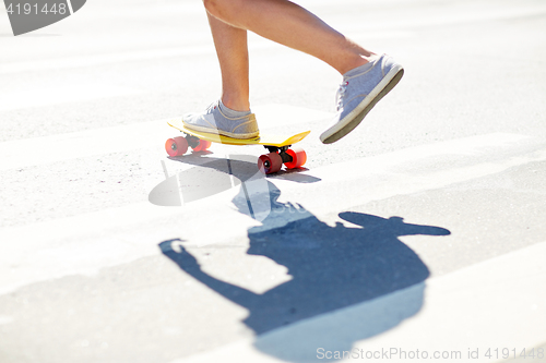 Image of male legs riding short skateboard along crosswalk