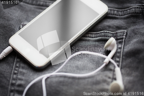 Image of smartphone and earphones on denim or jeans pocket