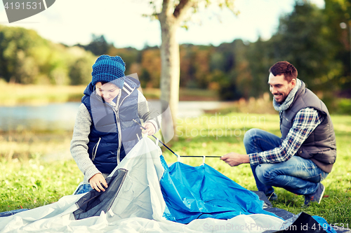 Image of happy father and son setting up tent outdoors