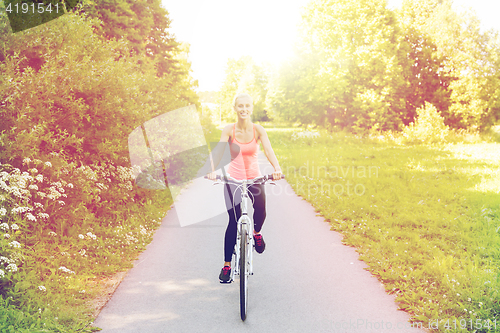 Image of happy young woman riding bicycle outdoors