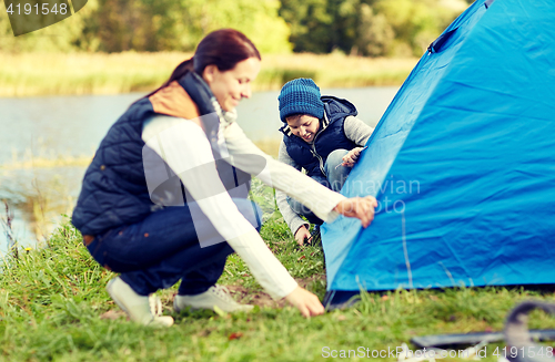 Image of happy mother and son setting up tent outdoors
