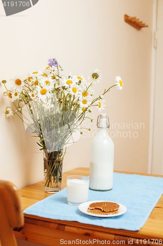 Image of Simply stylish wooden kitchen with bottle of milk and glass on table, summer flowers camomile, healthy foog moring concept